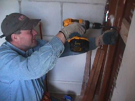 The plumber drills a wooden support brace for supporting copper pipes and fixtures in the wall behind the shower.