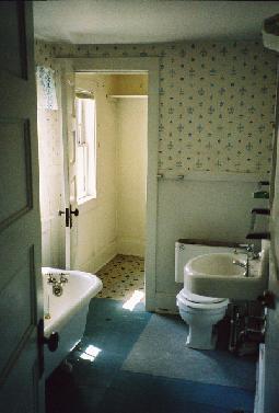long bathroom with claw-foot tub in foreground, toilet in rear, closet with window beyond