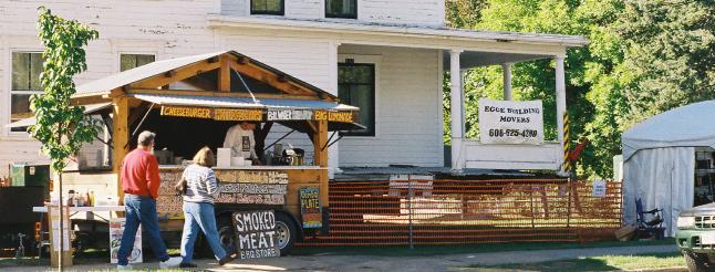 passersby, in longsleeves and trousers, examine festival vendors 
in front of the house