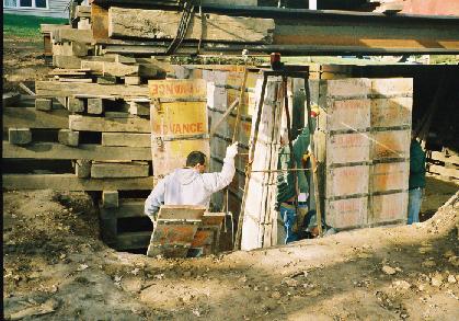closer view of workers setting up cement forms down in the basement excavation. 