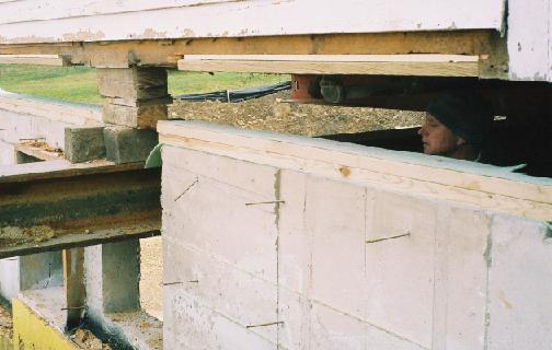 The carpenter keeps his eye on a header beam to be sure it lines up with the pocket in the foundation as the house slowly lowers