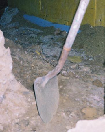 shovel in foreground in trench around basement wall which is covered by insulation with a drain tube running along the bottom of the wall