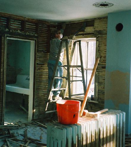 Scott, masked after pounding the dusty plaster off the walls, removes the exposed wooden lathwork above the kitchen window