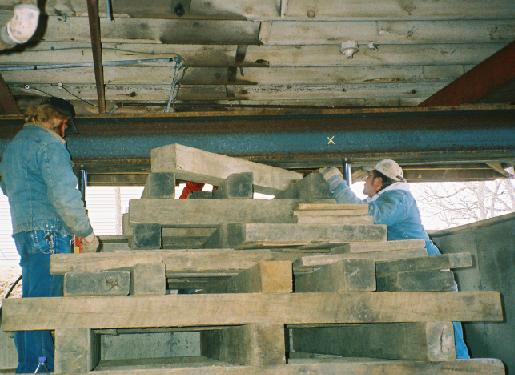 workers remove wooden beam below an I-beam which is supported by two hydraulic jacks on either side