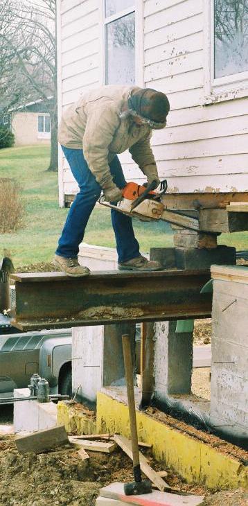 head of moving crew perched on an I-beam 5 feet above ground chain-sawing a header block to size