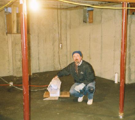 Ken kneels beside the propane jet heater on the newly poured concrete basement floor